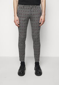 Pantalons à carreaux gris avec un motif écossais fin, accents rouges et ajustement sur mesure, portés avec des chaussures et des chaussettes noires.