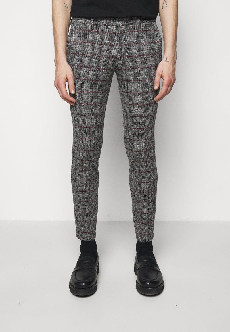 Pantalons à carreaux gris avec un motif écossais fin, accents rouges et ajustement sur mesure, portés avec des chaussures et des chaussettes noires.