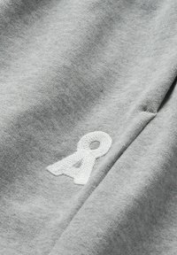 Gros plan sur un tissu gris avec un symbole en boucle brodé en blanc près d'une couture, montrant les détails de la texture et des points.