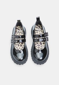 Zapatos de charol negros con dos correas de hebilla, punta redondeada y plantilla de leopardo. Suela de goma gruesa con relieve texturizado.