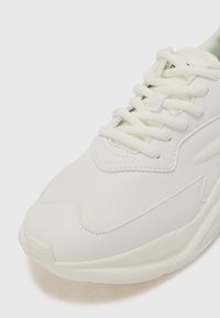 White sneaker with a textured, synthetic upper, featuring a lace-up design and a soft, cushioned sole. Includes subtle stitching details.