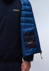 Námořnický fleece pulover s čtvrtzipem, spárovaný s modrou prošívanou bundou, která má kapsu a detail loga na rukávu.