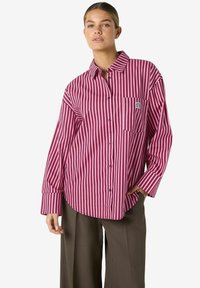 Long-sleeve, button-up shirt in burgundy and white vertical stripes. Features a chest pocket and relaxed fit with wide cuffs.