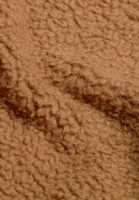Tessuto marrone texturizzato con una superficie morbida e pelosa e un motivo ondulato, simile a shearling o pile. Il materiale appare caldo e accogliente.