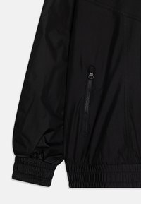 Black windbreaker jacket with elastic cuffs, featuring a zippered side pocket. Smooth material with a matte finish and a fitted design.