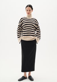 Pulover dungat în nuanțe de bej și negru, cu o croială supradimensionată și guler înalt; asortat cu o fustă lungă neagră și pantofi slip-on negri.