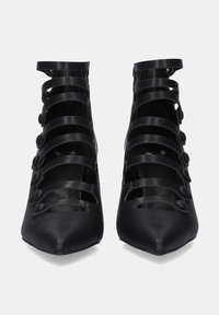 Zapatos de tacón negro con un diseño de punta afilada, que cuentan con múltiples correas horizontales y acentos de botones redondos en los laterales.