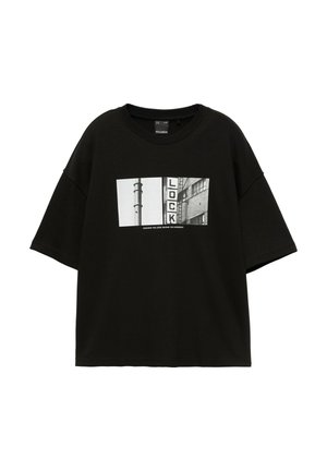T-shirt noir à manches courtes avec une photo rectangulaire en noir et blanc montrant un poteau, un bâtiment et un panneau "LOCK" en lettres majuscules épaisses.