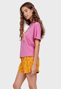 Roze katoenen T-shirt met korte mouwen en een speelse grafiek, gecombineerd met gele shorts met een zonnenpatroon, beide in een ontspannen fit en lichtgewicht.