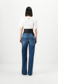 Witte T-shirt (korte mouwen) over een zwarte tailleband en blauwe high-waisted jeans. Heeft rechte pijpen en een ontwerp met een achterzak.