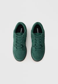 Tenisi verzi din suede cu un design low-top, având șireturi plate și o branț neagră în contrast. Vârf rotunjit și detalii texturate.