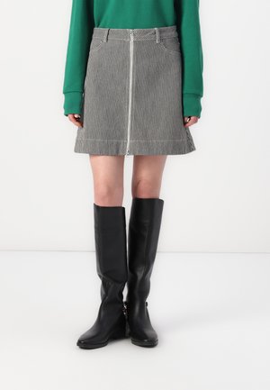 Black and white striped denim skirt with a front zip, paired with knee-high black leather boots. Green long-sleeve top visible.