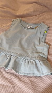 Svetlomodrý džínový top bez rukávov s peplum lemom, s okrúhlym výstrihom a viditeľnými švovými detailmi.