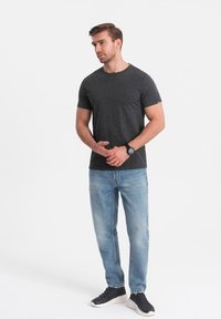 Mørkegrå prikket t-shirt med rund hals, parret med lyseblå denim jeans. Modellen har sorte sneakers og et mørkt ur på.
