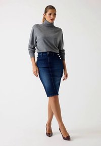 Grauer Rollkragenpullover kombiniert mit einem hoch taillierten, figurbetonten, dunkelblauen Denim-Bleistiftrock mit vier goldfarbenen Knöpfen auf der Vorderseite.