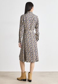 Rochie cu mâneci lungi, cu un model floral albastru și auriu, talie strânsă și fustă evazată. Asortată cu botine bej.