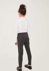 Weißes Langarmhemd mit Kragen, getragen zu grauen Leggings und schwarzen Slippers, von hinten betrachtet. Glatte Textur und taillierter Schnitt.