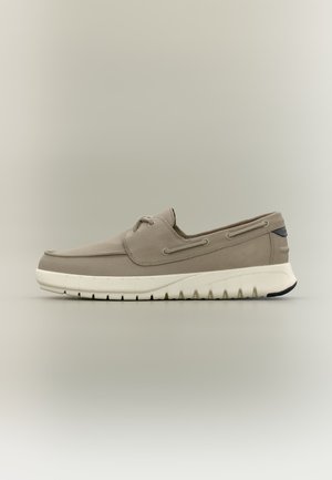 Beige casual boot met witte rubberen zool, veterluiting aan de voorkant en zijstikseldetails op een effen neutrale achtergrond.