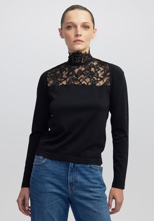 Haut noir à manches longues avec un col en dentelle haut et des détails en dentelle florale sur le devant. Le pull a une coupe ajustée et une texture lisse.