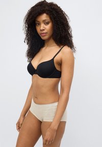 Μαύρο επενδεδυμένο σουτιέν με ρυθμιζόμενες τιράντες και λεπτομέρεια φιόγκου μπροστά, σε συνδυασμό με ανοιχτό μπεζ ελαστικά boyshorts με δαντέλα στο τελείωμα.
