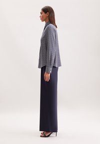 Blusa a motivi navali con maniche lunghe, polsini con bottoni e una vestibilità rilassata abbinata a pantaloni navy a vita alta e sandali neri con tacco.