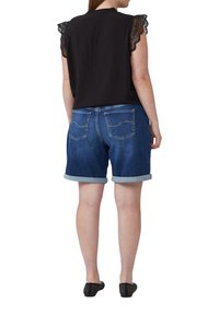 Haut noir sans manches avec des accents en dentelle, associé à un short en jean délavé avec des ourlets roulés et des poches arrière avec des coutures jaunes.