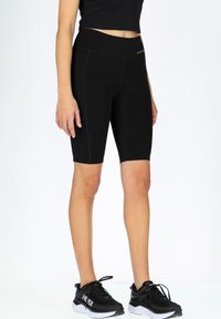 Svart cykelshorts gjorda av elastiskt material, med hög midja och slät yta, tillsammans med svarta träningsskor.