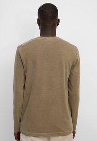 Langarmshirt aus beigem Baumwollstoff. Verfügt über einen Rundhalsausschnitt, geraden Schnitt und genähten Saum. Weiche Textur ohne sichtbare Muster oder Verzierungen.