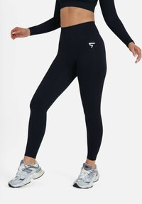 Navy high-waisted leggings with a textured pattern and a small white logo on the thigh, paired with gray athletic shoes.