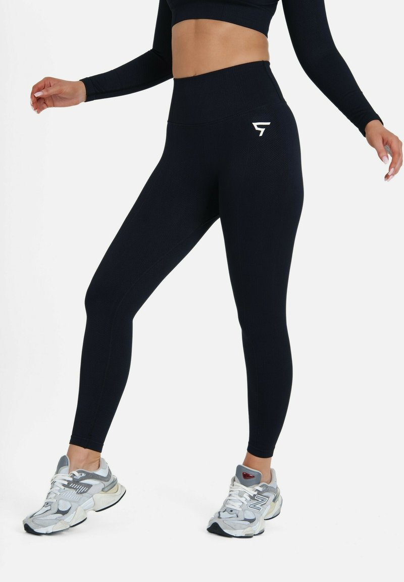 Navy hoge taille leggings met een gestructureerd patroon en een klein wit logo op de bovenbeen, gecombineerd met grijze sportschoenen.