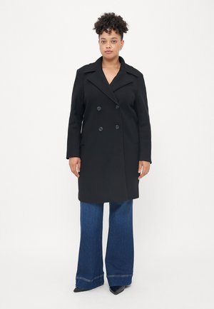 Manteau croisé en mélange de laine noir avec de larges revers, poches latérales, coupe droite et manches longues, associé à un jean bleu évasé.