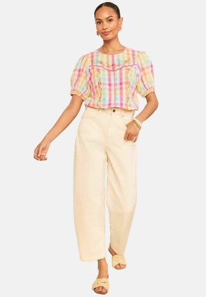 Kvinde iført en pastelternet bluse med puffede ærmer og blomsterbroderi, cremefarvede vidde bukser, flettede slip-on sandaler og armbånd.