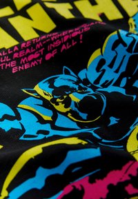 Graafilise kujundusega t-särk, millel on must kangas ja erksad sinised, kollased ning roosad koomiksistiilis pildid, sealhulgas julged tegelased ja tekstielemendid.