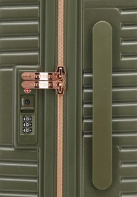 Valise rigide verte avec une texture à nervures verticales, fermetures éclair en bronze et un cadenas à combinaison pour renforcer la sécurité.