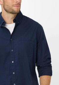 Marineblauwe button-up shirt met een omgeslagen kraag, één borstzak en opgerolde mouwen. Zachte stof met een gladde textuur en een getailleerde pasvorm.