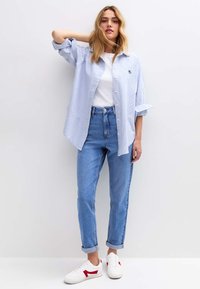 Lichtblauw-wit gestreept overhemd met opgerolde mouwen, gecombineerd met lichtgewassen jeans met hoge taille en witte sneakers met rode accenten.