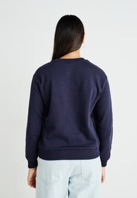 Sweatshirt azul marinho com gola redonda e punhos canelados, feito de um tecido suave, combinado com calças de ganga azul claro.