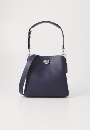 Sac à main en cuir bleu marine avec bandoulière réglable et fermeture à boucle argentée à l'avant, présenté sur un fond blanc uni.