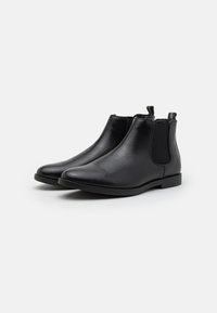 Botas Chelsea de piel negra con paneles laterales elásticos, punteras redondeadas y suelas planas para un uso fácil. Presentan altura hasta el tobillo y lengüetas para facilitar el calzado.