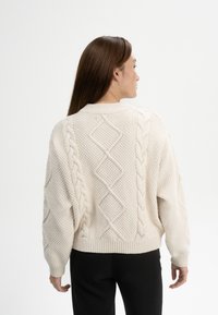 Kuscheliger, cremefarbener Strickpullover mit Kabelmuster, Rautentexturen und gerippten Bündchen. In einem verkürzten, lässigen Schnitt gestaltet.