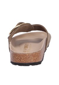 Sandal in suede marrone con un accento circolare dorato, soletta in sughero e suola nera testurizzata. La vista posteriore mostra il rivestimento interno liscio e la forma sagomata.