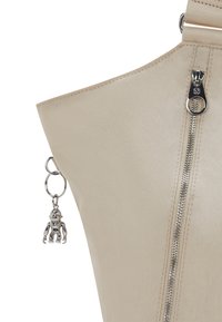Beige l�äderhandväska med en texturerad yta, utrustad med en silverdragkedja och en metallberlock i form av en figur.