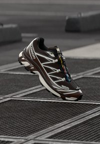 Dark brown running shoe with white and multicolored accents, textured upper, and flexible sole, featuring a quick-lace system and reinforced toe.