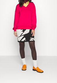 Roze sweatshirt met V-hals, rok met zwart-wit patroon, donkere kousen, witte sokken en oranje schoenen. Soepele stof en een comfortabele pasvorm.