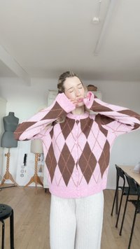 Rosa-brauner Argyle-Cardigan mit langen Ärmeln und Knopfverschluss, mit strukturierter Strickart und großzügiger Passform. Kombiniert mit weißen, gerippten Hosen.