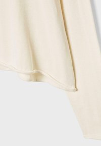 Pull en maille couleur crème avec une texture douce et lisse, montrant l'ourlet et les bords des manches sur un fond blanc.