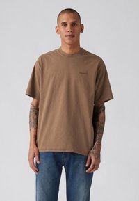 Bruine katoenen t-shirt met ronde hals en korte mouwen, voorzien van een subtiele, ingedrukte logo op de borst. Draag het met blauwe denim jeans.