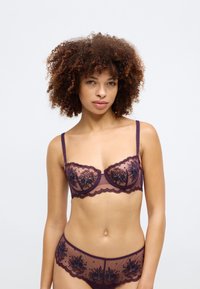 Lace lingerie set in deep purple with floral embroidery, featuring a structured bra with underwire and matching lace brief. Sheer texture.
