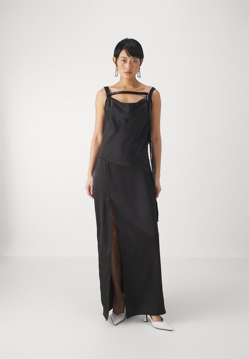 Rochie din satin negru, cu o deschidere laterală, design asimetric și detalii cu bretele. Încălțămintea constă în tocuri albe ascuțite. Textură netedă, stil minimalist.