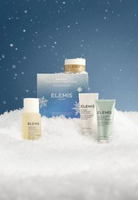 Ensemble de produits de nettoyage posé sur une surface semblable à de la neige. Comprend un pot doré, trois tubes blancs et verts, et une boîte bleue avec un motif de flocon de neige.